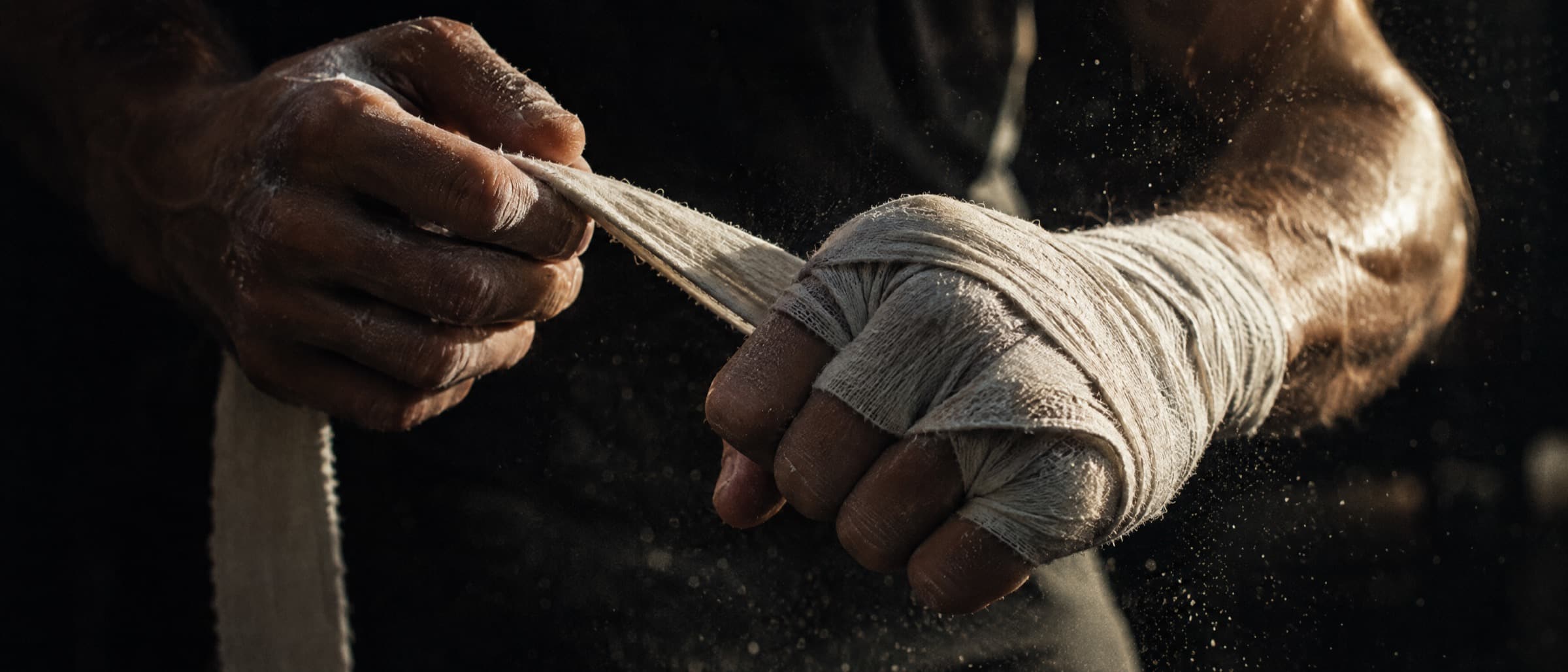 A fighter's hands wrapping white hand wraps in warm side light